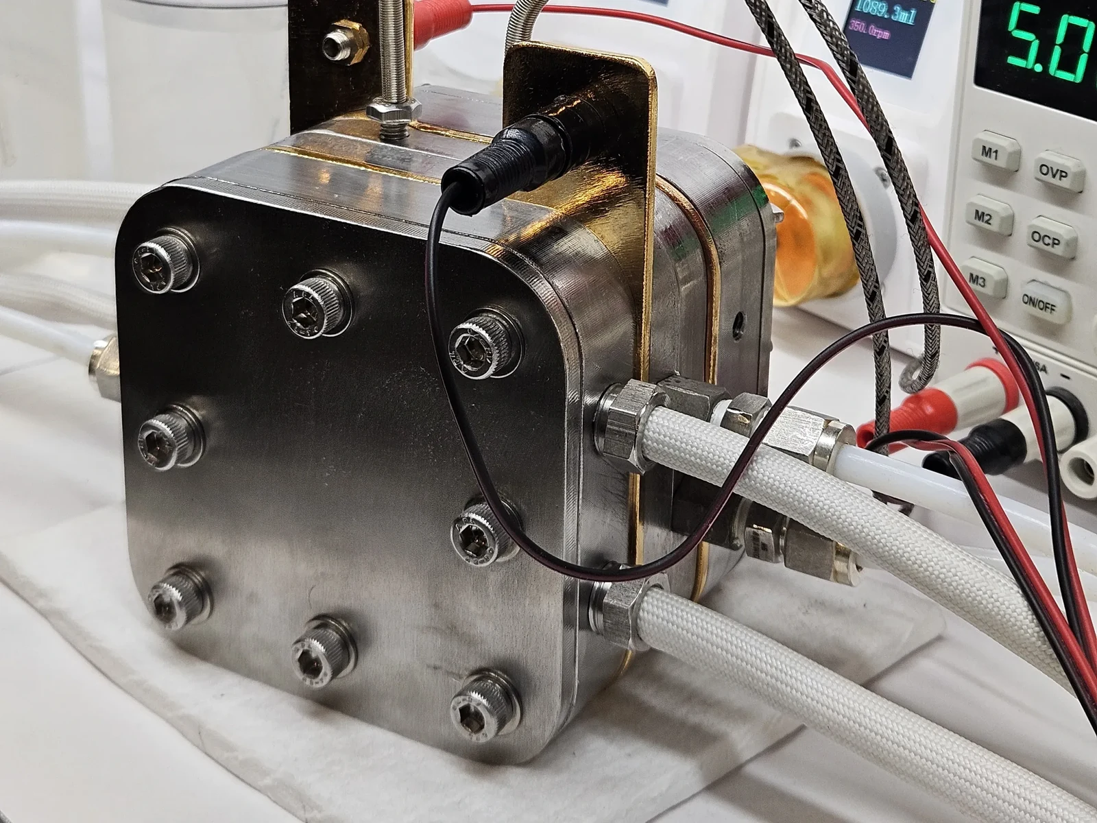 High Temperature PEM/AEM Electrolyzer Hardware - the cell on the bench with its power leads connected and a bench supply behind